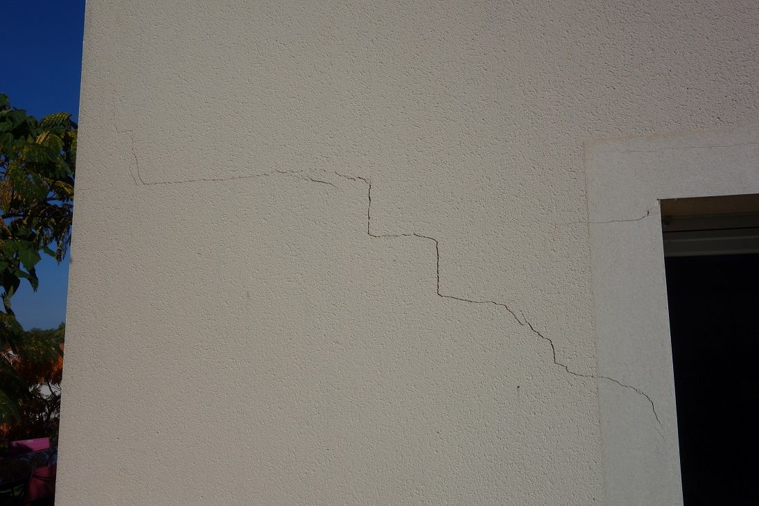 fissure en forme d'escalier sur l'enduit d'une maison neuve